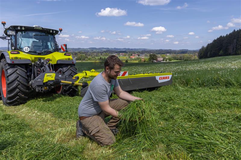 Mann der im Feld die Ernte begutachtet, mit Claas Traktur im Hintergrund
